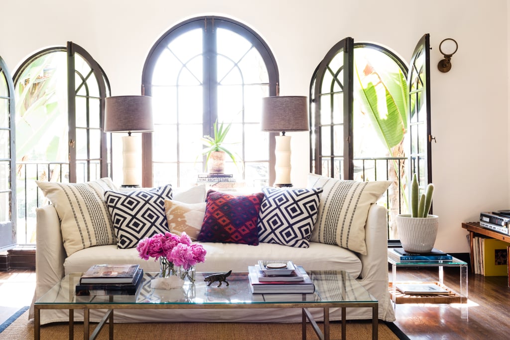 A glass coffee table and lucite side tables make for an airy feel, while graphic pillows mirror the architectural details of the windows.