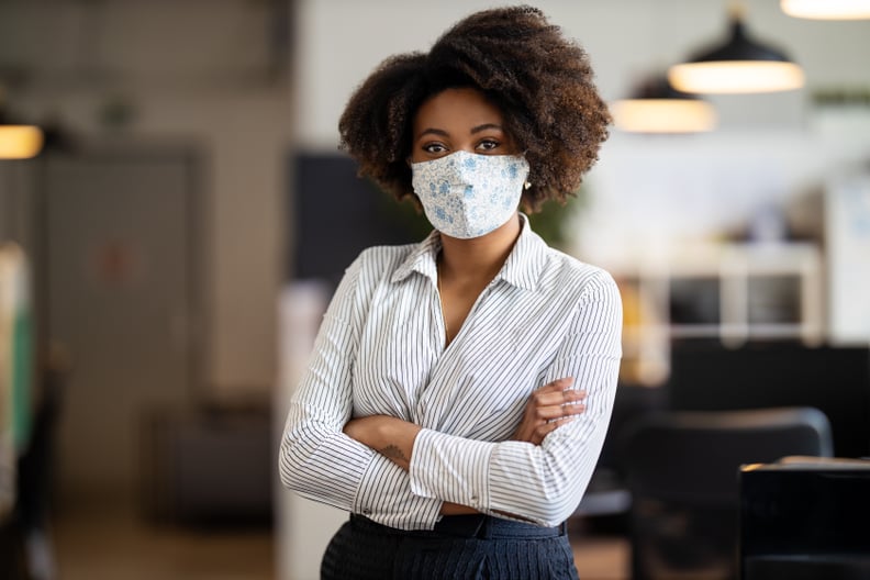 Portrait of african american businesswoman back to work at office after pandemic lockdown. Female entrepreneur with protective face mask standing alone in office with her arms crossed.