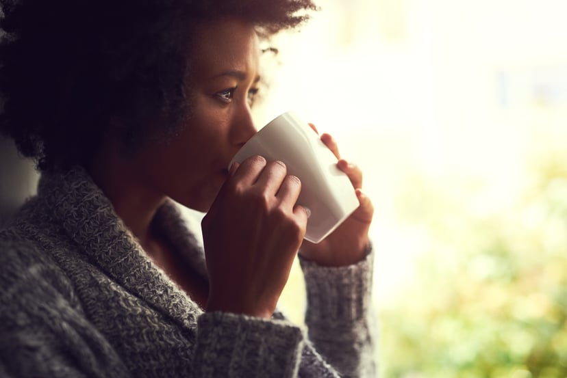 Shot of a relaxed young woman enjoying a cup of coffee while sitting by a window at home