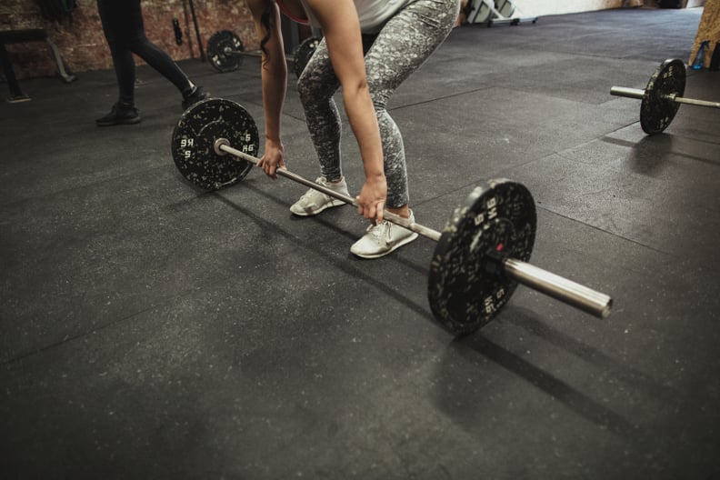 Female cross training ter using a barbell to prefrom a deadlift while at a gym.