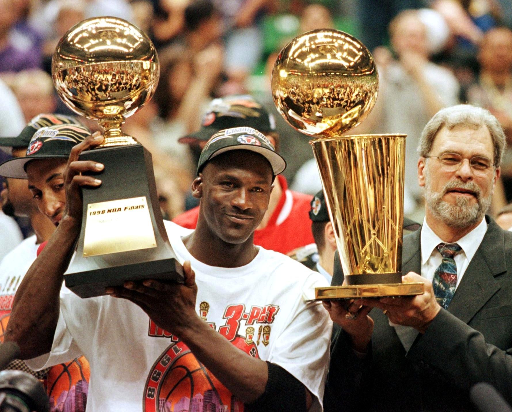 (FILES) In this 14 June 1998 file photo, Michael Jordan (L) holds the NBA Finals Most Valuable Player trophy and former Chicago Bulls head coach Phil Jackson holds the NBA champions Larry O'Brian trophy 14 June after winning game six of the NBA Finals with the Utah Jazz at the Delta Centre in Salt Lake City, UT. The Bulls won the game 87-86 to take their sixth NBA championship. Jackson left the Bulls following the 1998 season and 12 January reports indicate that Jordan plans to announce his retirement at a 13 January news conference in Chicago.   AFP PHOTO/FILES/Jeff HAYNES (Photo by JEFF HAYNES / AFP) (Photo by JEFF HAYNES/AFP via Getty Images)