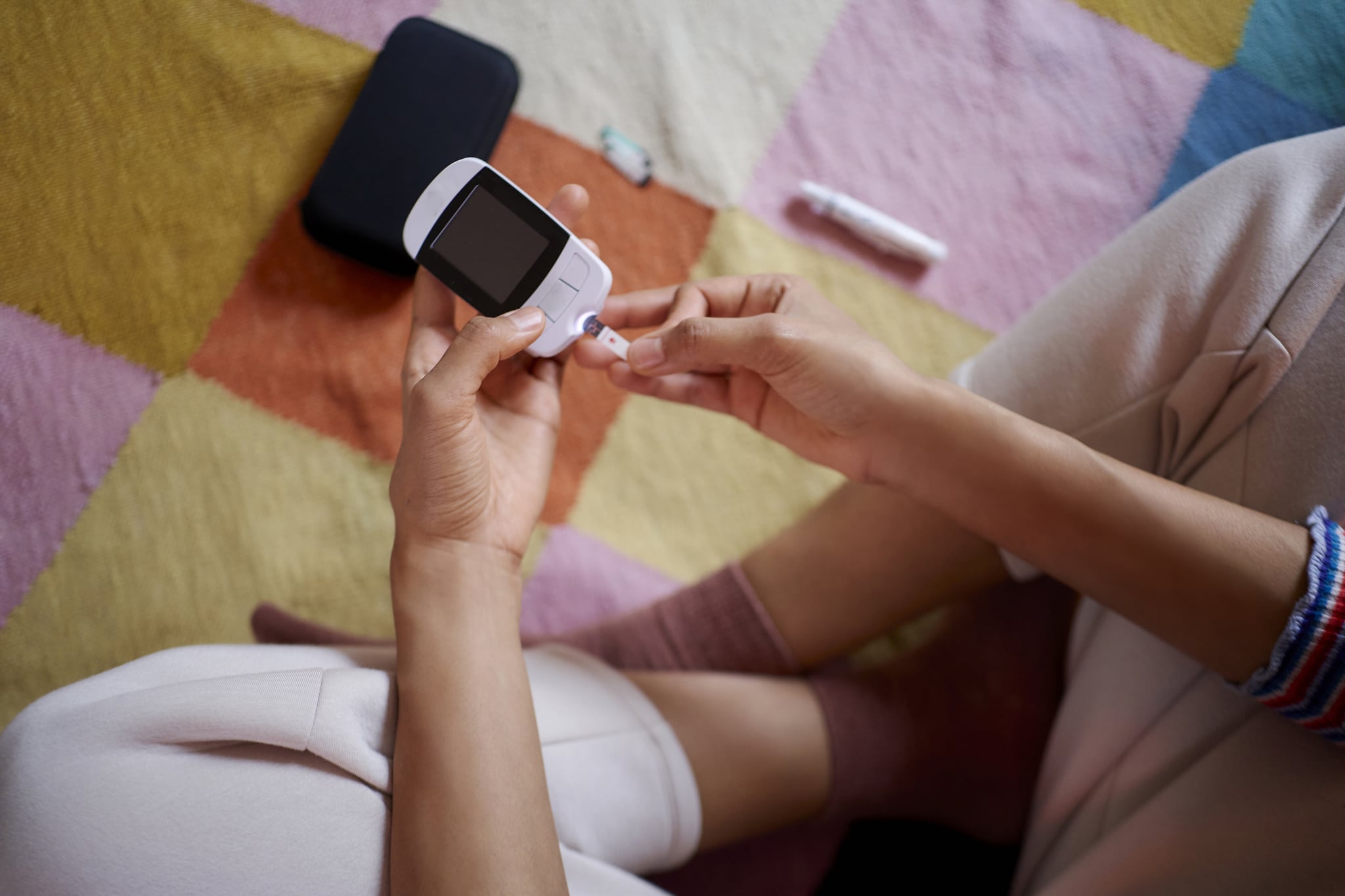 Young woman measuring her blood sugar using glucometer sitting on carpet in the living room.