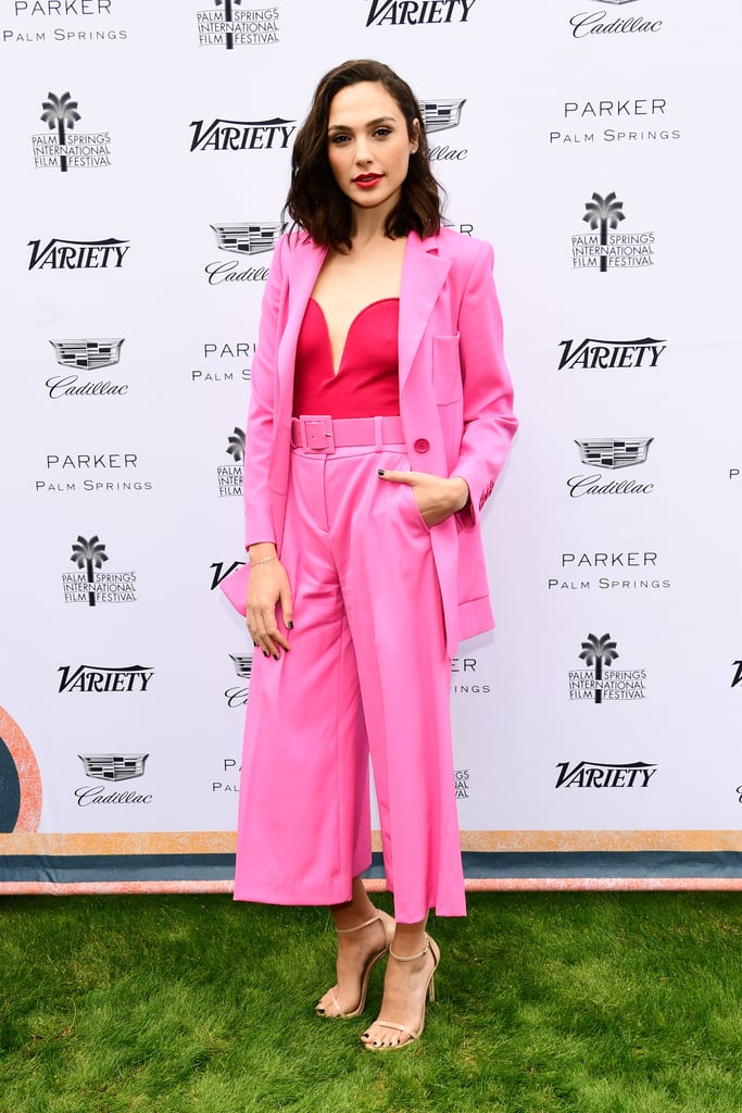 When Gal Gadot isn't in her Wonder Woman armor, she's rocking the brightest outfits IRL on the red carpet. After wearing a yellow Esteban Cortazar dress at the Palm Springs Film Festival, the star arrived to another event in a magenta suit. The Oscar de la Renta two-piece outfit consisted of an oversize blazer, which Gal wore unbuttoned, and a pair of flared, culotte-style pants.  
Underneath her ensemble, Gal gave up a bra to wear a red strapless bodysuit and added an extrasweet touch to her outfit with a red bracelet. The accessory benefits her friend's foundation, which helps children suffering from genetic metabolic diseases.
It was hard to ignore such a strong look, which, no doubt, her stylist, Elizabeth Stewart, had a hand in creating. Elizabeth has an eye on the latest trends, and pairing red and pink together is what every fashion girl will be doing in 2018. Plenty of street style stars test drove the look already, and Gal is all on board for the bright color combination. As award season heats up, keep your eyes on the star and her many stylish outfits.