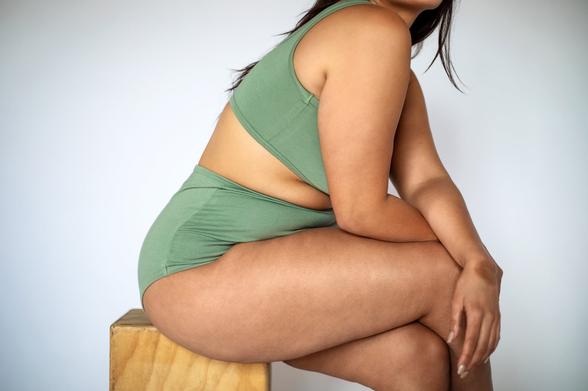 Woman in green underwear and bra set sitting on a stool to represent green discharge.