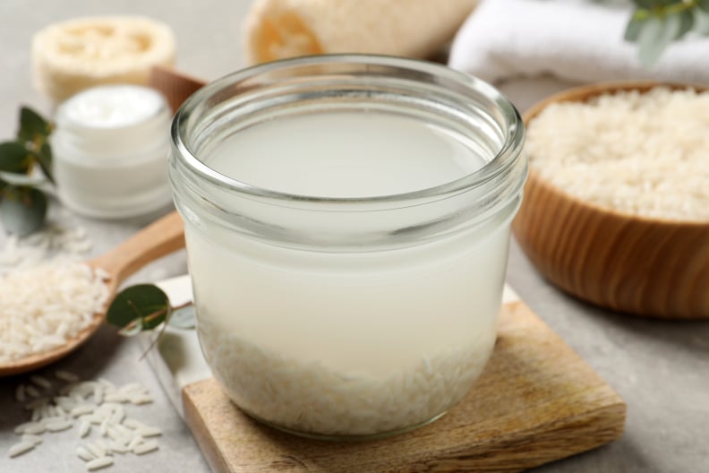 Glass jar with uncooked rice soaked in water on a light grey table with a bowls full of uncooked rice in the background.