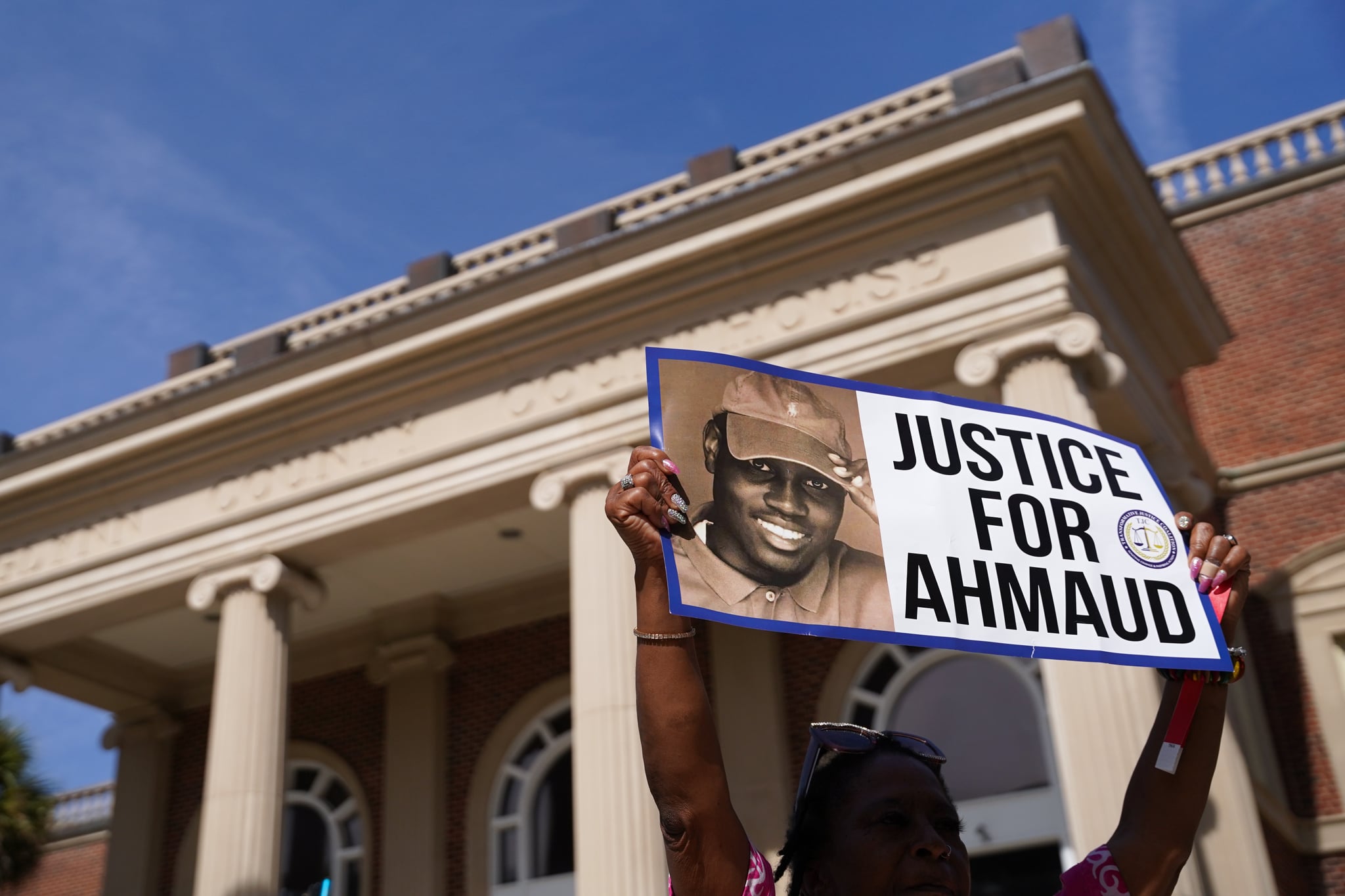 BRUNSWICK, GA - OCTOBER 18: A demonstrator holds a sign at the Glynn County Courthouse as jury selection begins in the trial of the shooting death of Ahmaud Arbery on October 18, 2021 in Brunswick, Georgia. Three white men are accused of chasing down and murdering Arbery in southeastern Georgia last year. (Photo by Sean Rayford/Getty Images)