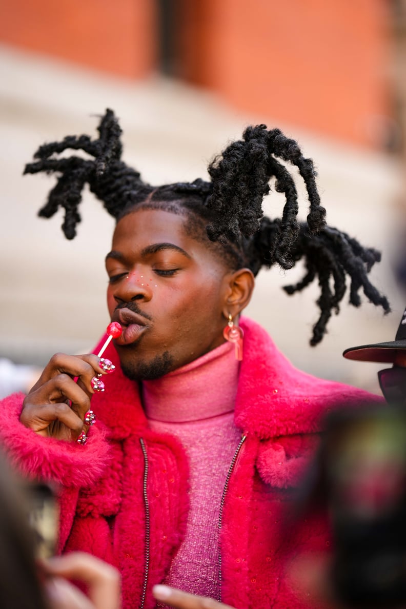 NEW YORK, NEW YORK - FEBRUARY 13: Lil Nas X wears red pendant earrings, a pink glitter wool turtleneck pullover, a red fluffy oversized long coat, outside Coach, during New York Fashion Week, on February 13, 2023 in New York City. (Photo by Edward Berthel