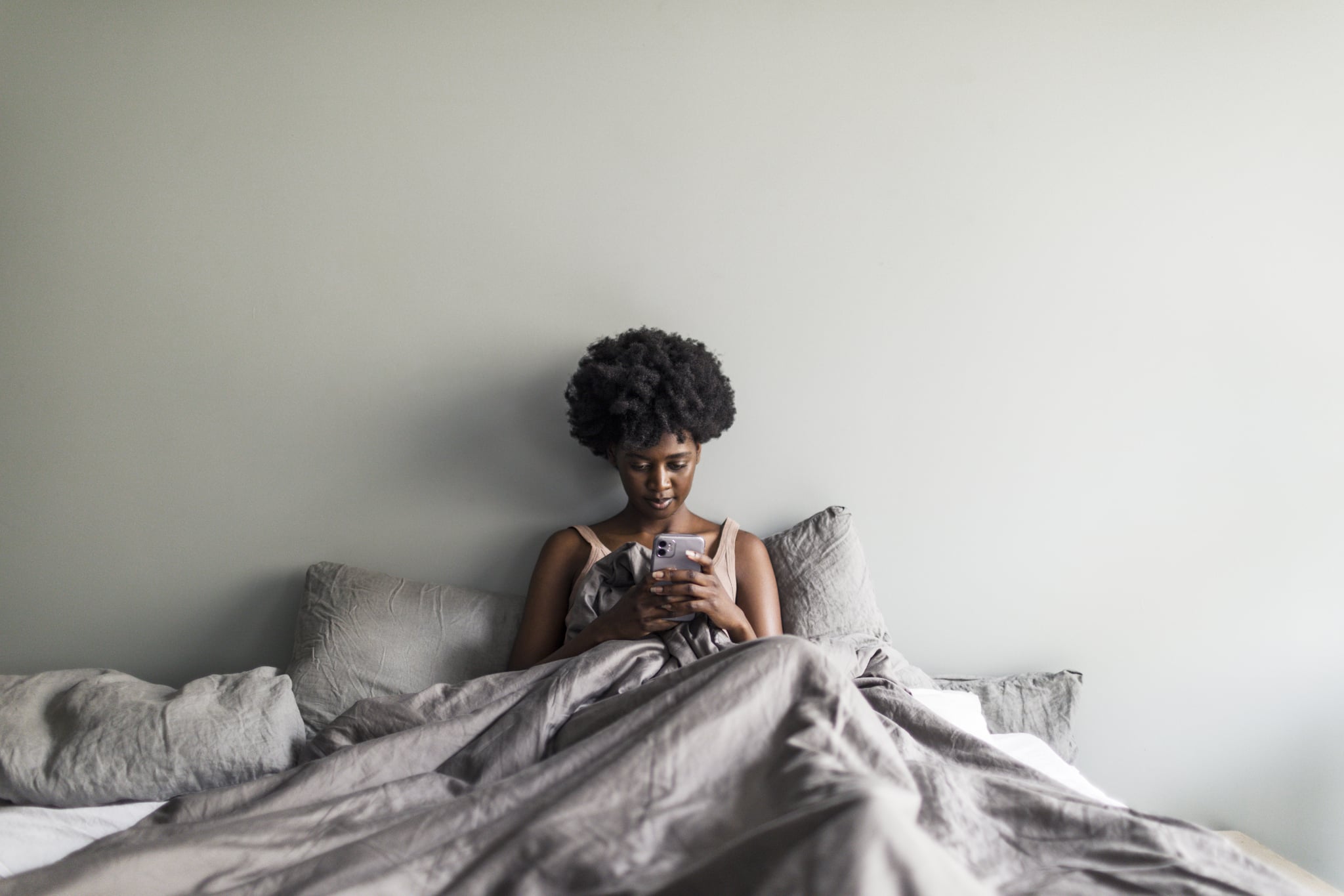 Young adult black woman reading news in the morning on mobile in bed