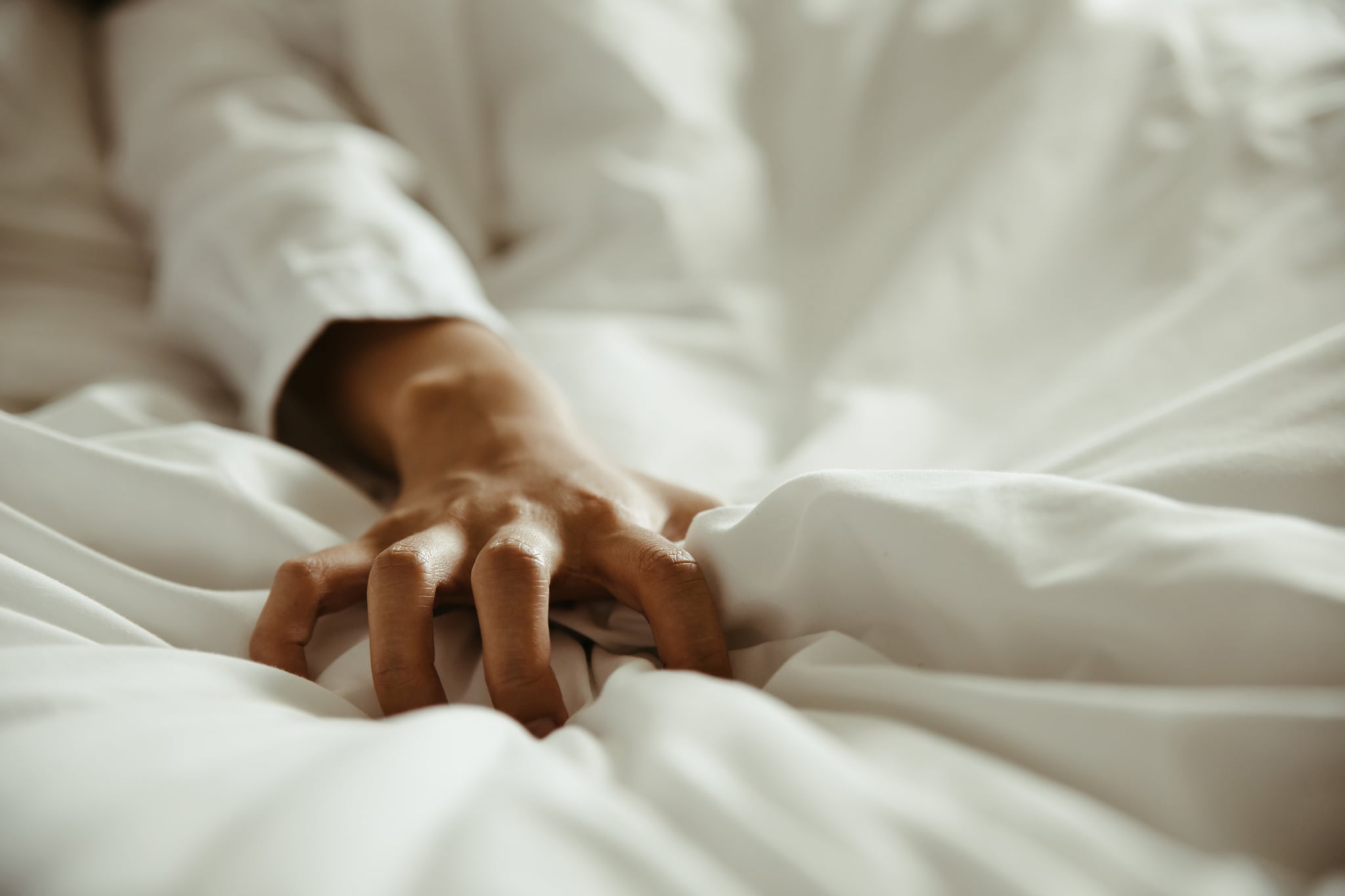 Close up of a woman's hand as she pulls on white sheets in ecstasy.