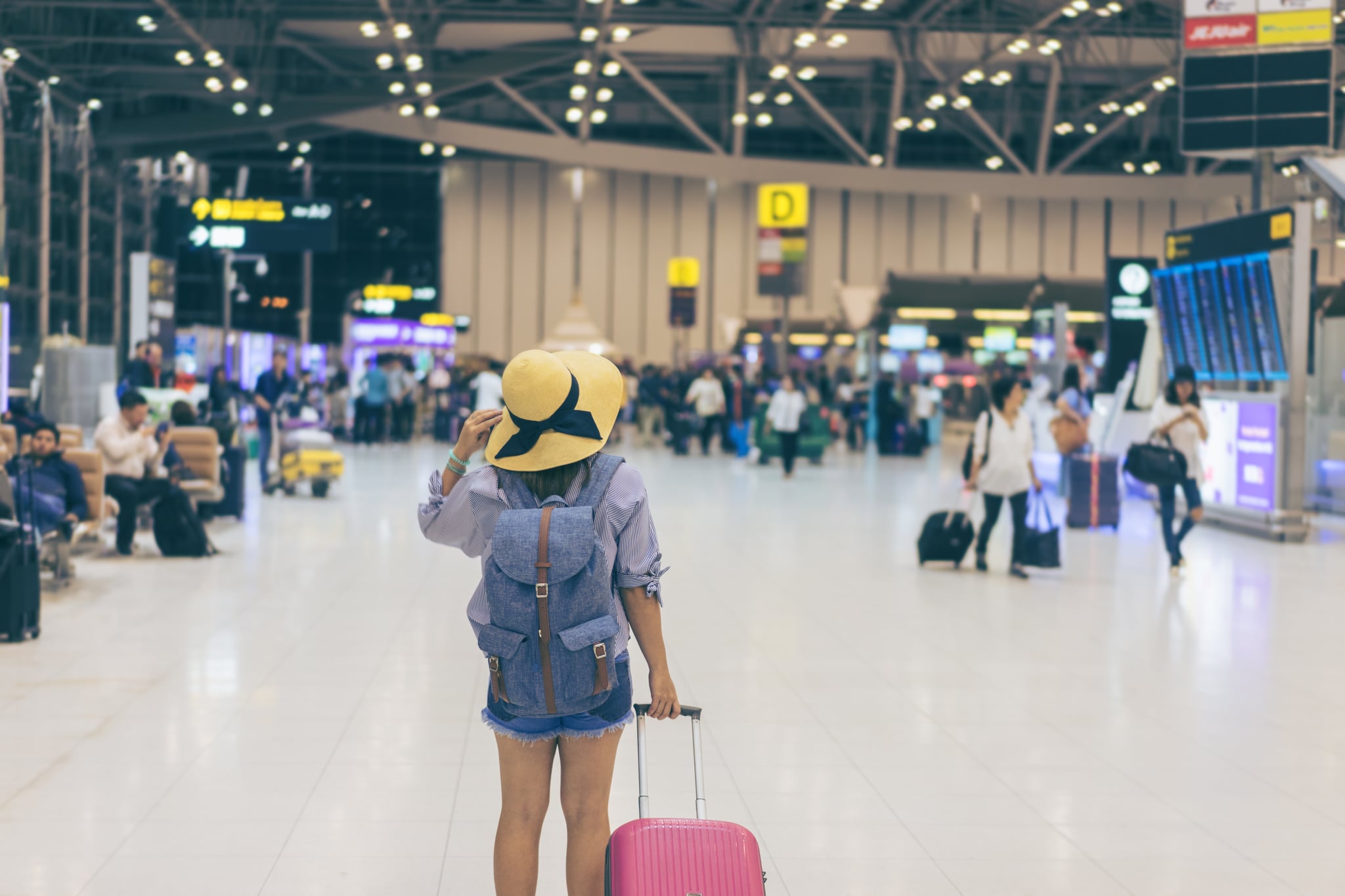 Young woman traveller in international airport with backpack holding suitcase or baggage in her hand, Beautiful young tourist girl with backpack and carry on luggage in airport terminal, on travelator