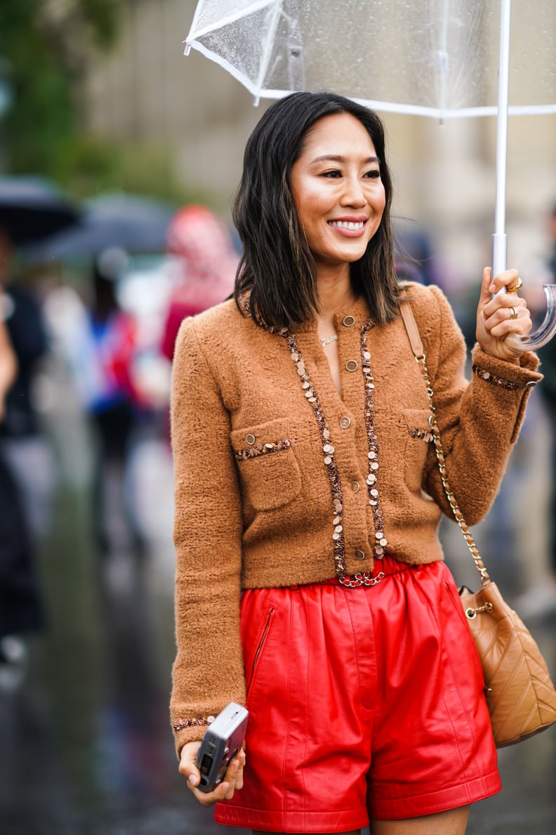 PARIS, FRANCE - OCTOBER 01: Aimee Song wears a brown wool jacket, red leather shorts, a light brown quilted bag, holds an umbrella under the rain, outside Chanel, during Paris Fashion Week - Womenswear Spring Summer 2020, on October 01, 2019 in Paris, Fra