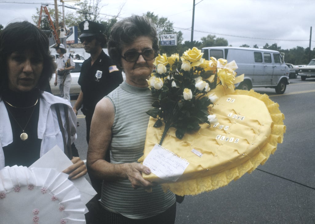 An older woman carries a flower arrangement that says, "We love you, Elvis."