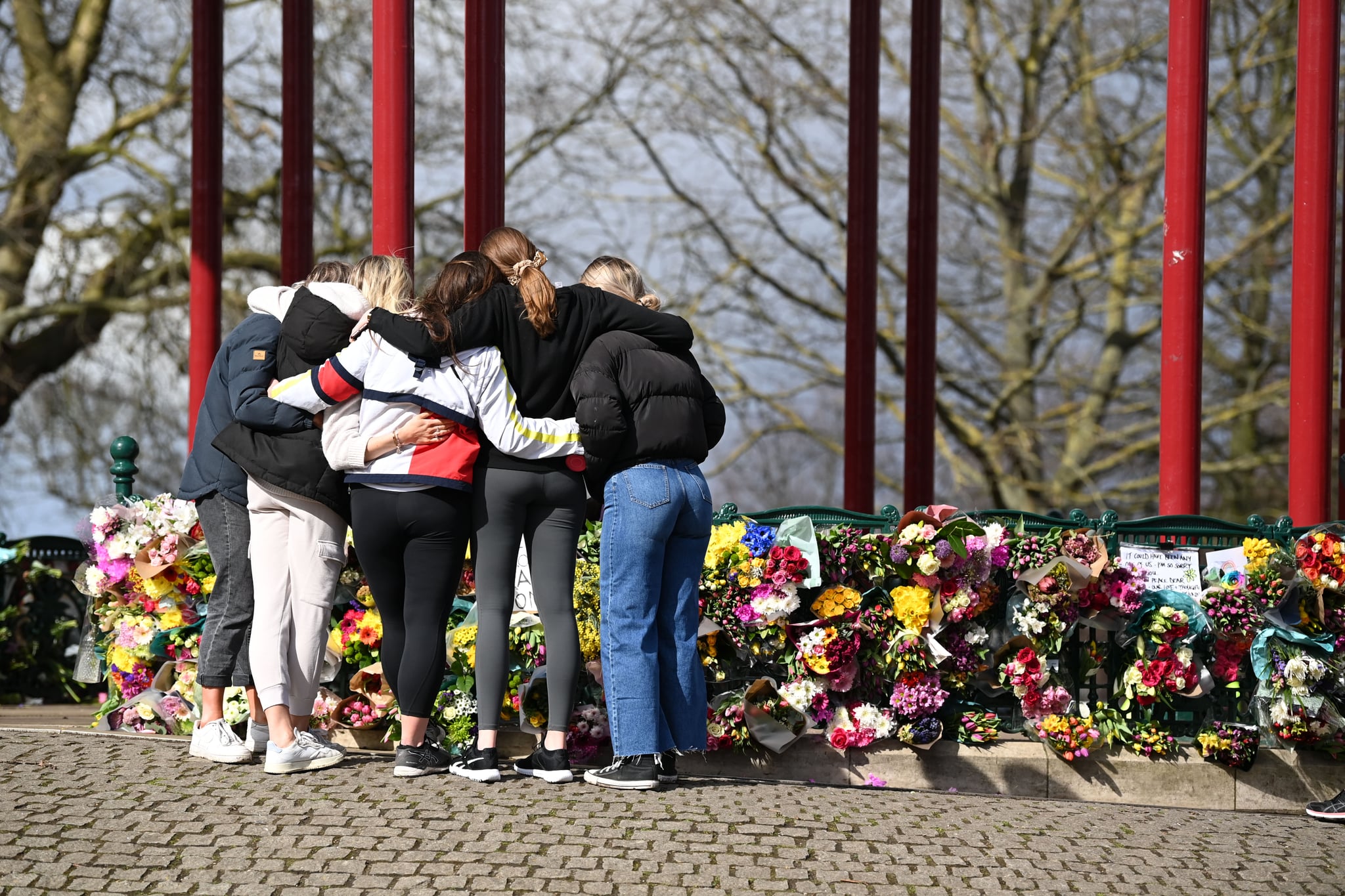 LONDON, ENGLAND - MARCH 13: A group of women hug as they stand in front of tributes for Sarah Everard at the bandstand on Clapham Common on March 13, 2021 in London, United Kingdom.  Vigils are being held across the United Kingdom in memory of Sarah Everard. Yesterday, the Police confirmed that the remains of Ms Everard were found in a woodland area in Ashford, a week after she went missing as she walked home from visiting a friend in Clapham. Metropolitan Police Officer Wayne Couzens has been charged with her kidnap and murder. (Photo by Leon Neal/Getty Images)