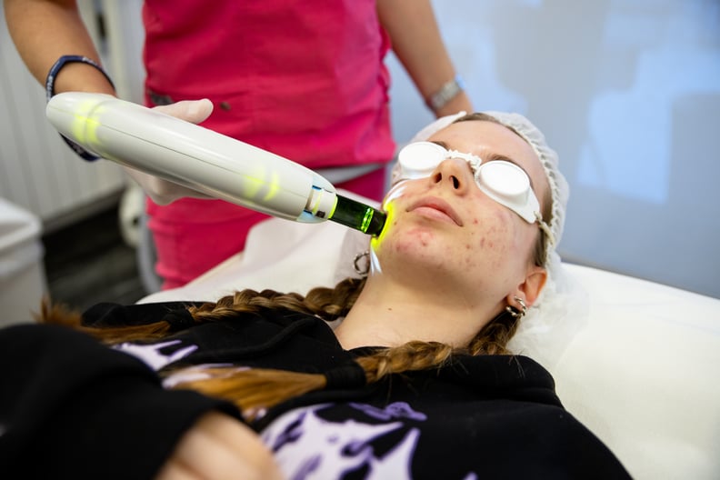 Laser light treatment for the teenage female skin face with pimples problem. Dermatologist in beauty clinic doing Carbon face skin cleaning to a teen girl