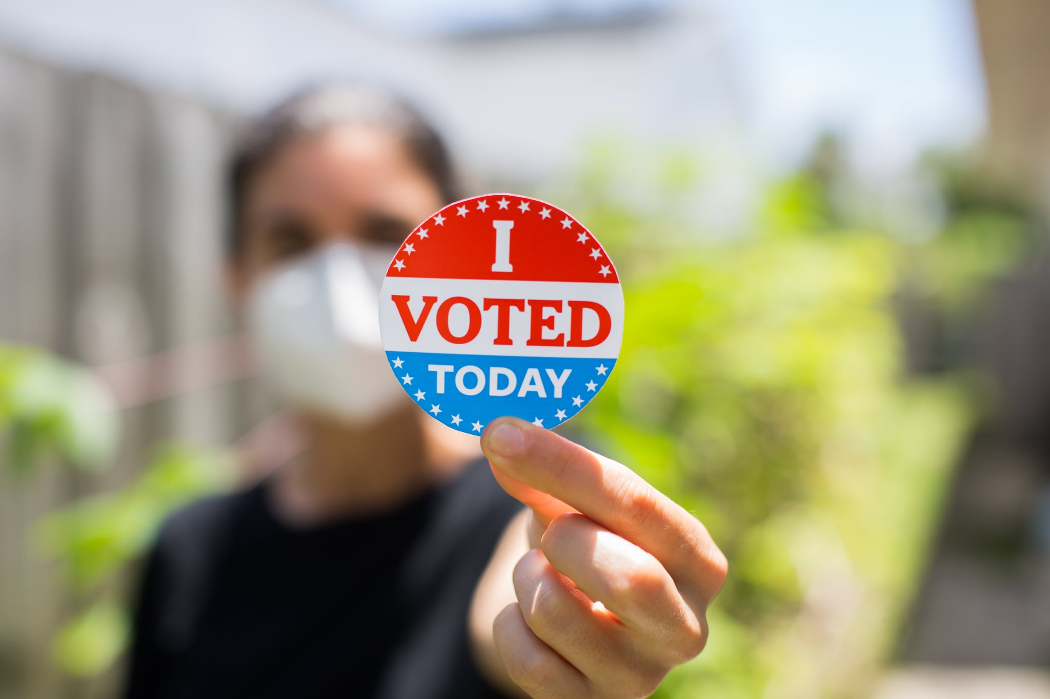 Young woman wearing face mask holding I voted today sticker.