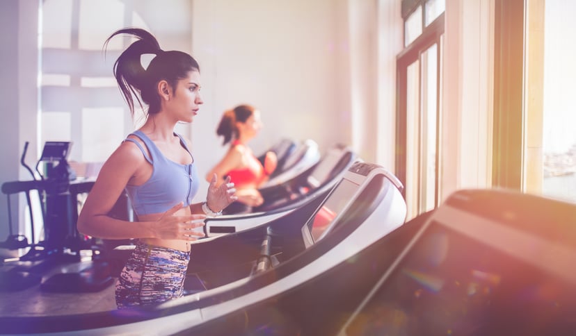 Young sporty hispanic woman running on treadmill and doing workout at fitness health club