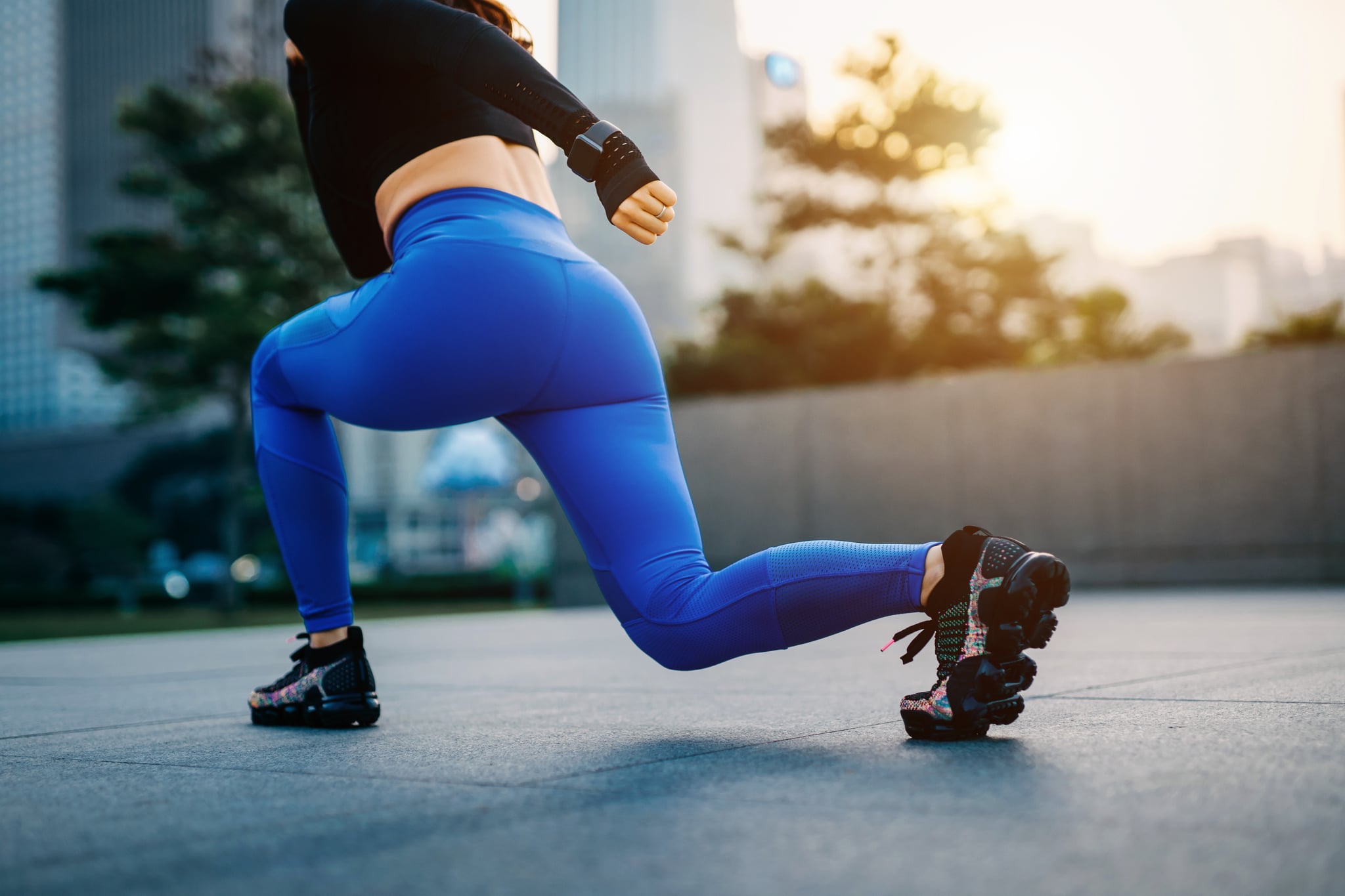 Close up of young sports woman stretching legs outdoors against urban cityscape at sunset