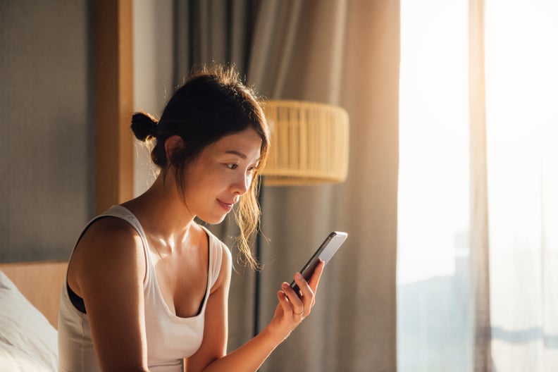 Portrait of young Asian woman holding smartphone while waking up in bed in the morning.