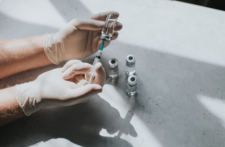 一只手戴着乳胶手套举行一个小玻璃瓶的透明液体和一个注射器。医学专业使用注射器从玻璃瓶中提取药物。概念空间复制。
