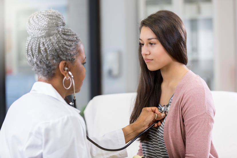 Female doctor uses stethoscope to listen to teenage girl's heartbeat.
