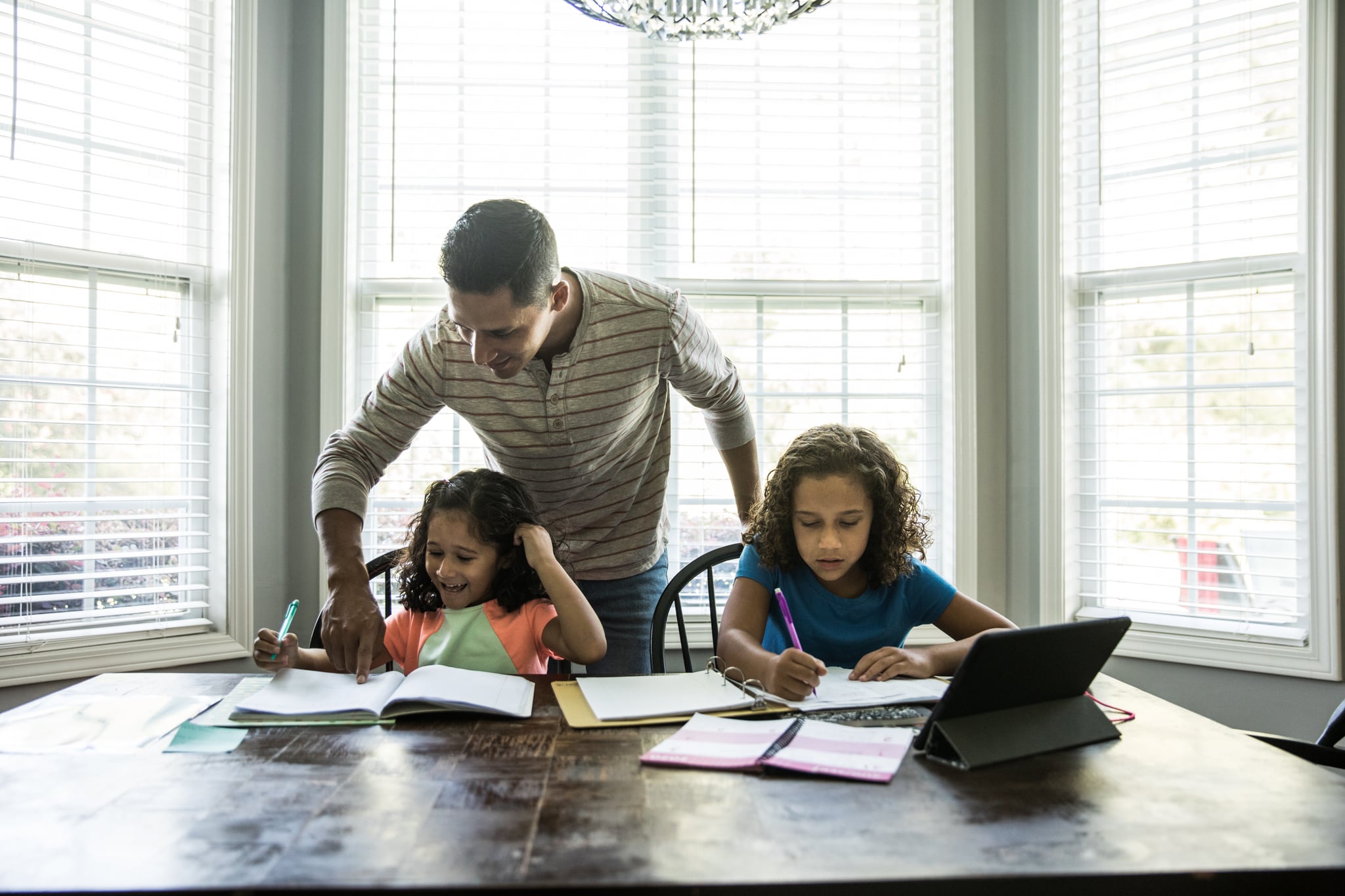 Father helping young girls with schoolwork at kitchen table