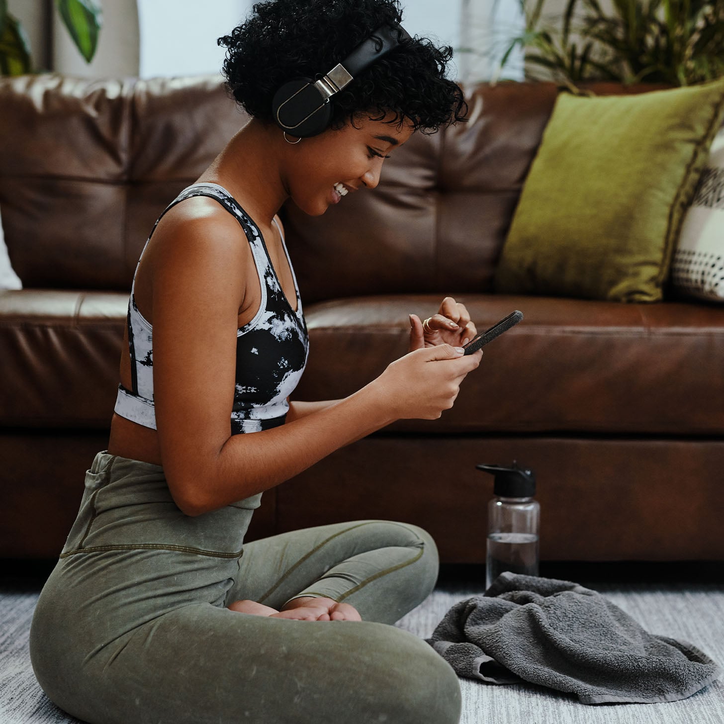 woman sitting on the floor in workout clothes making up a workout playlist name on her phone
