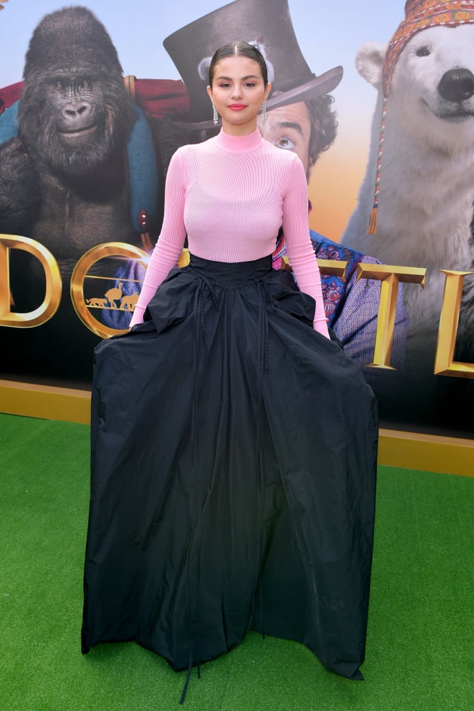 In another bold fashion move, Selena Gomez demands fans "look at her now" while wearing Givenchy at the premiere for Dolittle. Fresh off of her Rare album release, the 27-year-old performer walked the red carpet alongside her costars Rami Malek and Robert Downey Jr, and her voluminous black skirt certainly stole the show. Does anyone else get ballgown vibes from the dramatic gathered fabric?
This couture ensemble comes courtesy of Selena's stylist, Kate Young. She tied the look together with a pink turtleneck from the high-end designer and sparkling Messika jewelry. How chic! Selena appeared in good spirits as she posed for pictures, wearing complementary rose-colored lipstick and pastel eye shadow. Pretty in pink, indeed. Ahead, see more glimpses of Selena's look from all angles.