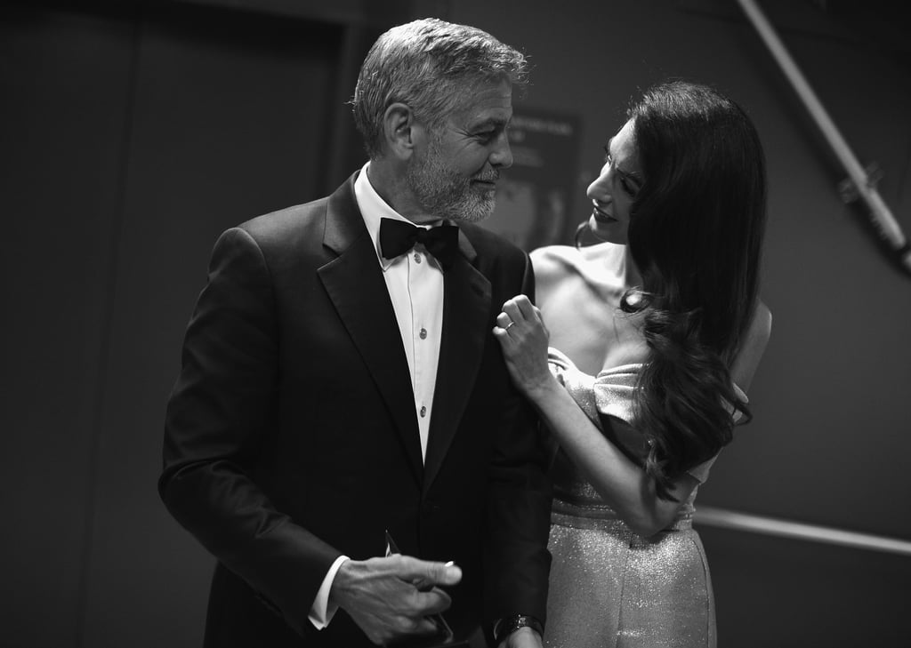 Following glamorous appearances at the Met Gala and then the royal wedding, we're starting to realize that George and Amal Clooney don't have regular date nights. In their latest outing, the couple appeared at the AFI Life Achievement Award Gala Tribute on Thursday in LA. In fact, the 57-year-old actor was the guest of honor as this year's recipient of the esteemed award.
Looking like they just stepped out of Old Hollywood, George wore a classic tuxedo, while Amal wore a dazzling pink — dare we say rose gold? — gown. The pair, parents to twins Alexander and Ella, looked like they had a great time, too, as they giggled all along the red carpet and lovingly looked at each other in that way they often do. 
The star-studded affair also brought out George's nearest and dearest including his parents, Nick and Nina Clooney, as well as Cindy Crawford, Rande Gerber, Jennifer Aniston, and Courteney Cox. Unfortunately, George and Amal's twins, Alexander and Ella, didn't make an appearance, but George did gush to Us Weekly about how they celebrated their first birthday on Wednesday. "Well, the kids got drunk. I don't know what you guys were doing, but I came home, they had a bottle of booze," George joked. "It was really embarrassing, but they're feeling better today."
George also opened up about his new life as a dad, saying, "It's really fun. It's perfect." Aw! Ahead, enjoy pictures from their classy evening.