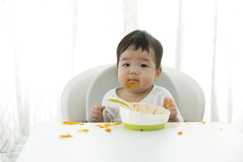 Asian baby learning self feeding on white background.