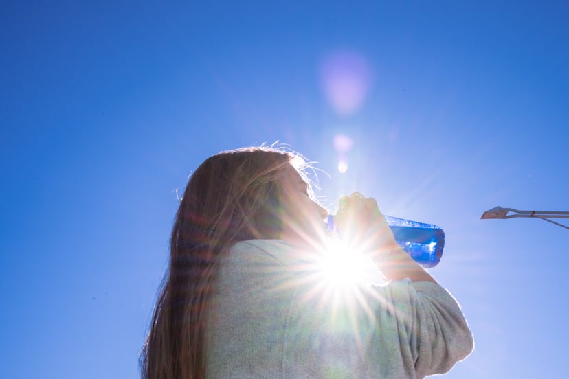 Blonde woman drinking water outside while being illuminated by a ray of sunlight.