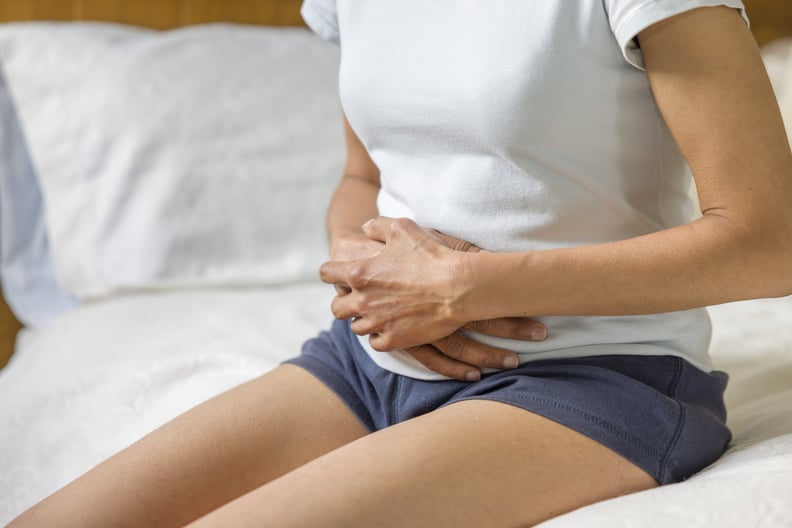 Woman sitting on bed, holding hormonal belly.