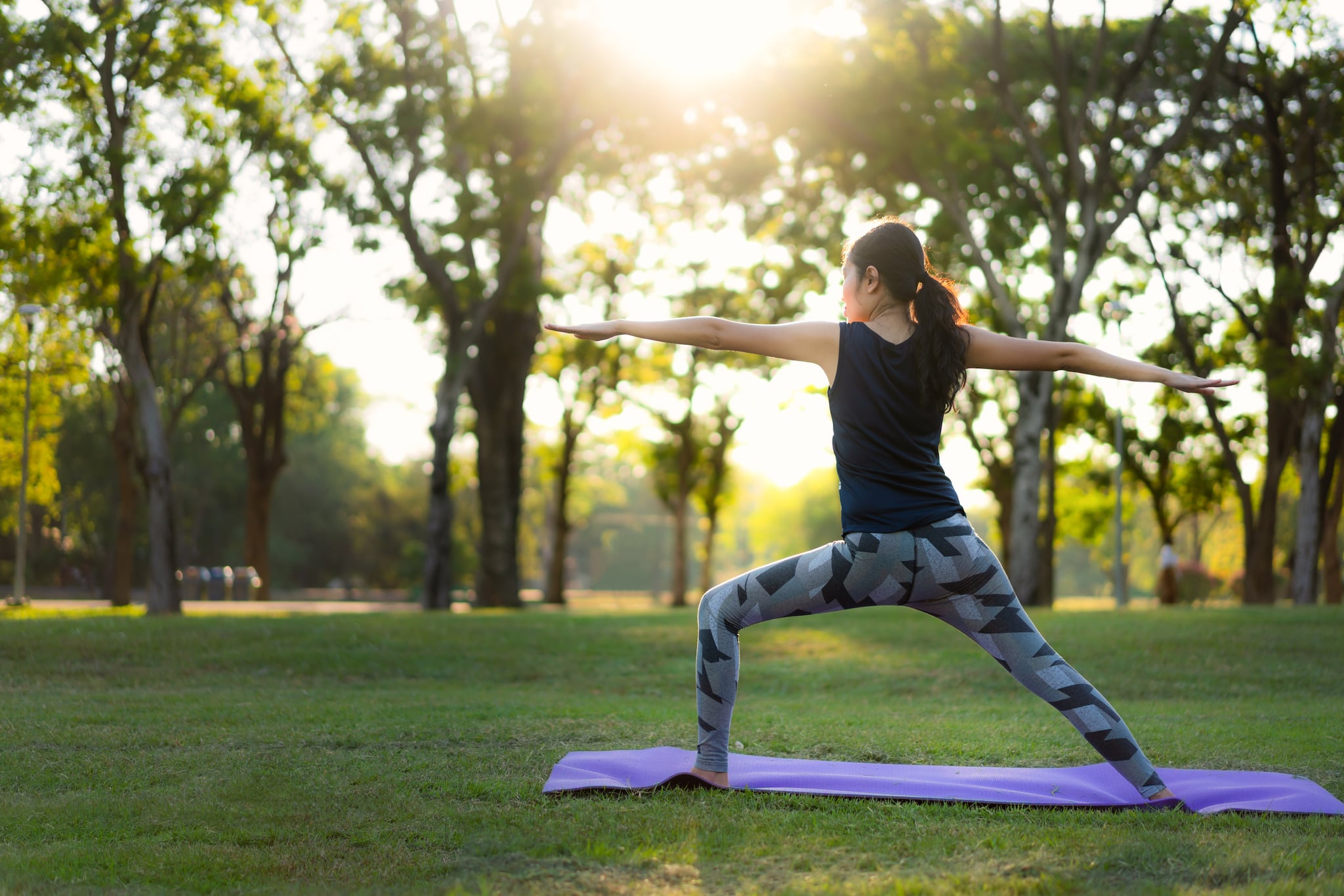 Young Aisan woman practicing yoga in park at sunset.