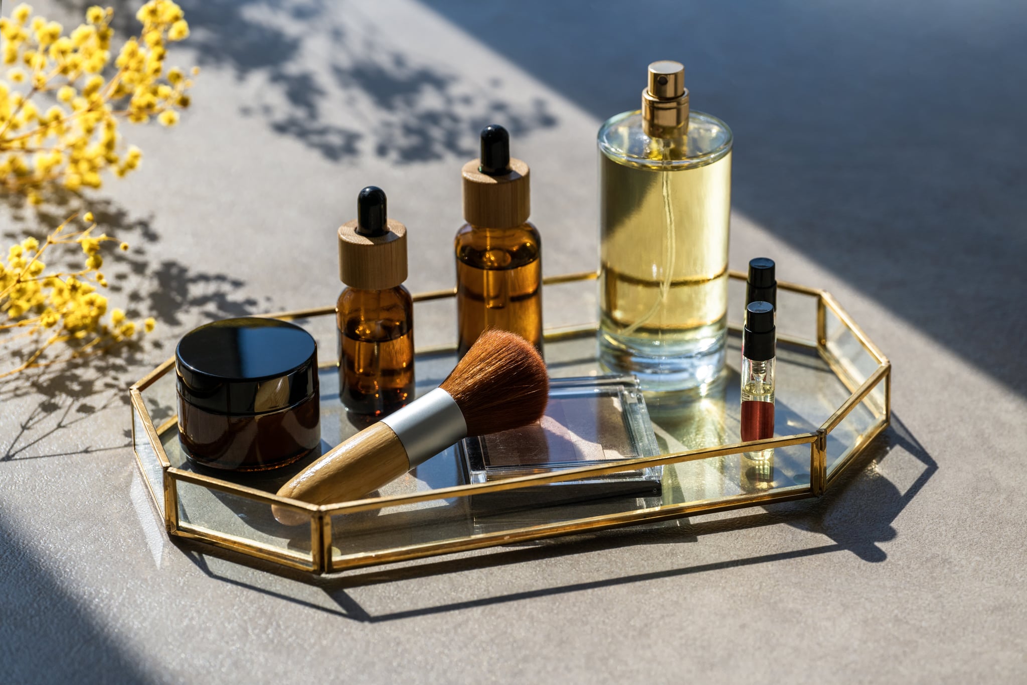 Cosmetic products on table in glass tray. Makeup brush and highlighter or shadows. Unrecognizable bottles of perfume and samplers. Dropper bottle with oils or serum for face and body care. Beauty concept