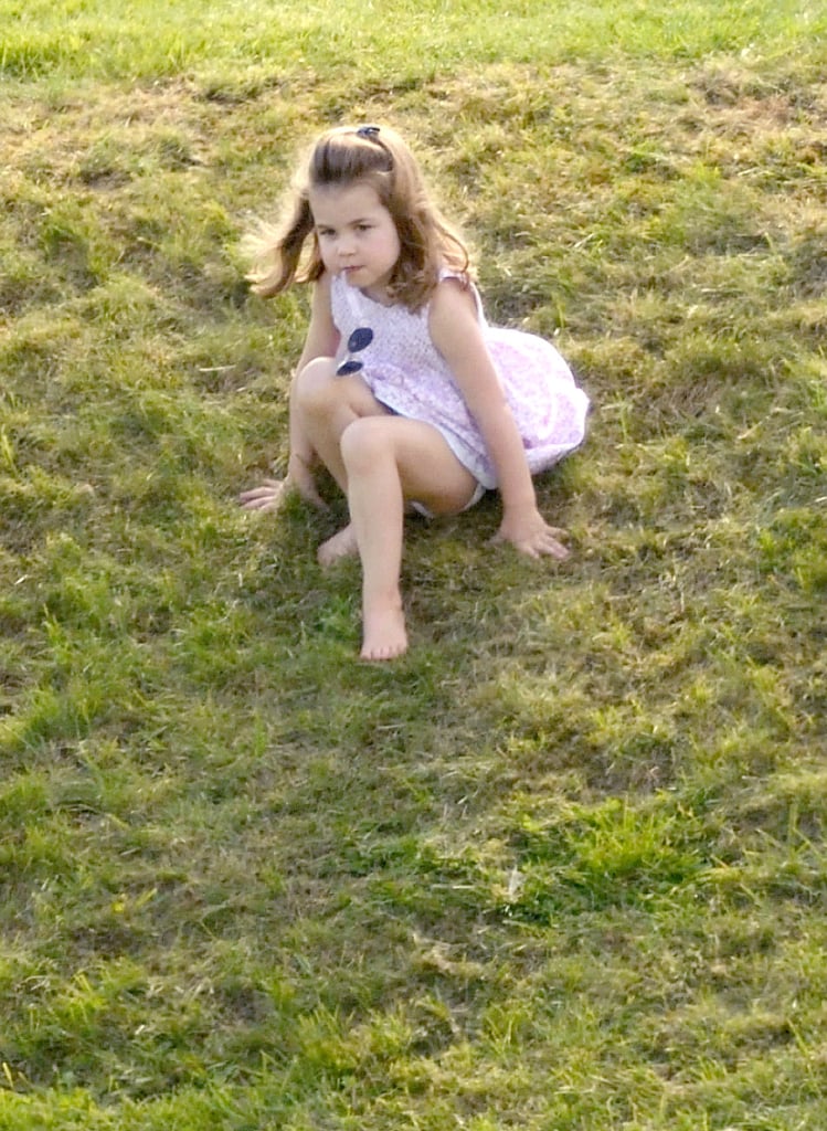 Princess Charlotte slides down a grassy hill in a sleeveless pink dress with her sunglasses in tow.