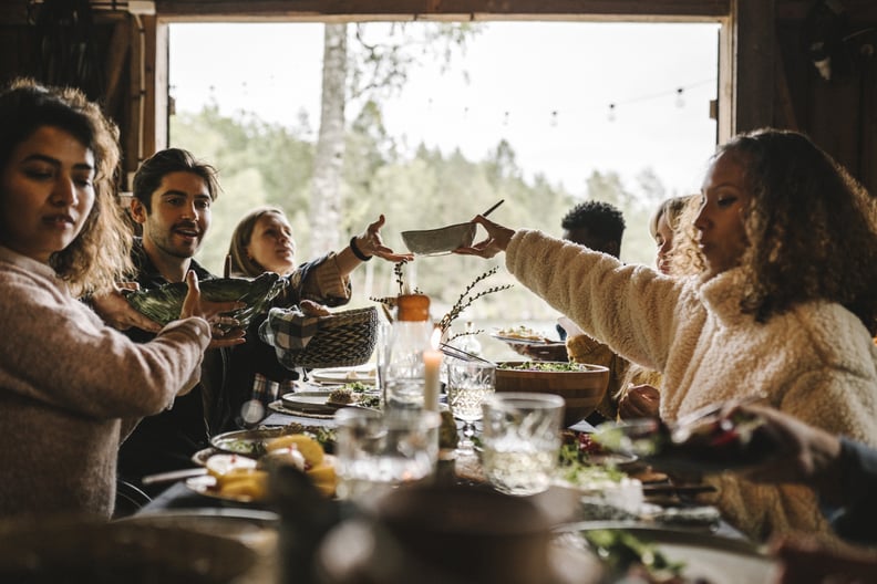 A group of young adults sit at a dinner party and pass food around.
