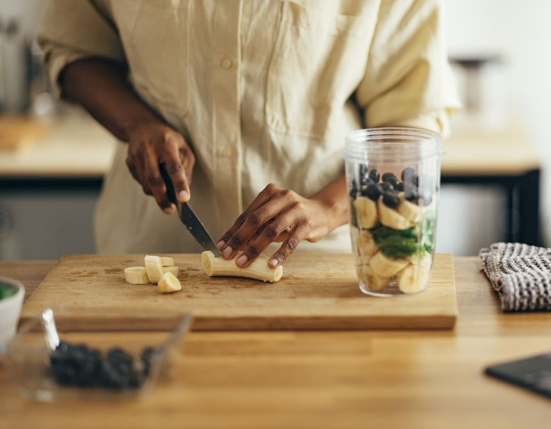 African American woman cutting banana making a smoothie, wondering about how many carbs are in a banana