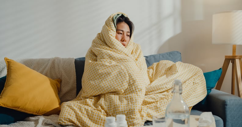 Woman with cold sweats, sitting on the sofa wrapped in a blanket.