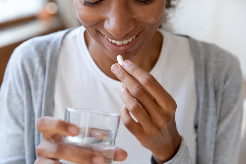 关闭快乐年轻的非洲裔美国年轻女性每日服用剂量的复杂的医疗保健皮肤,头发和指甲ω维生素喝一杯新鲜的纯水,免疫力提高的概念。