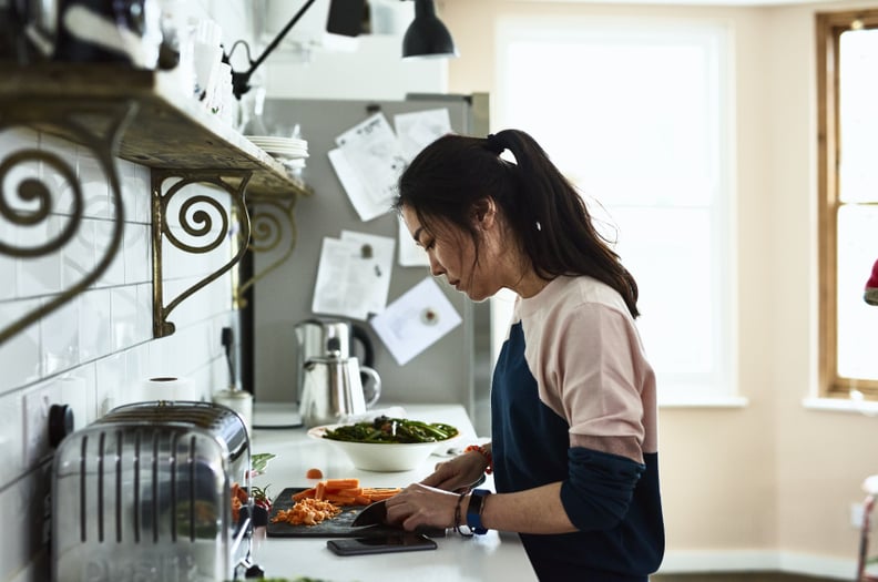 Side view portrait of attractive Asian woman in her 30s, cutting carrots on chopping board, concentrating and using knife