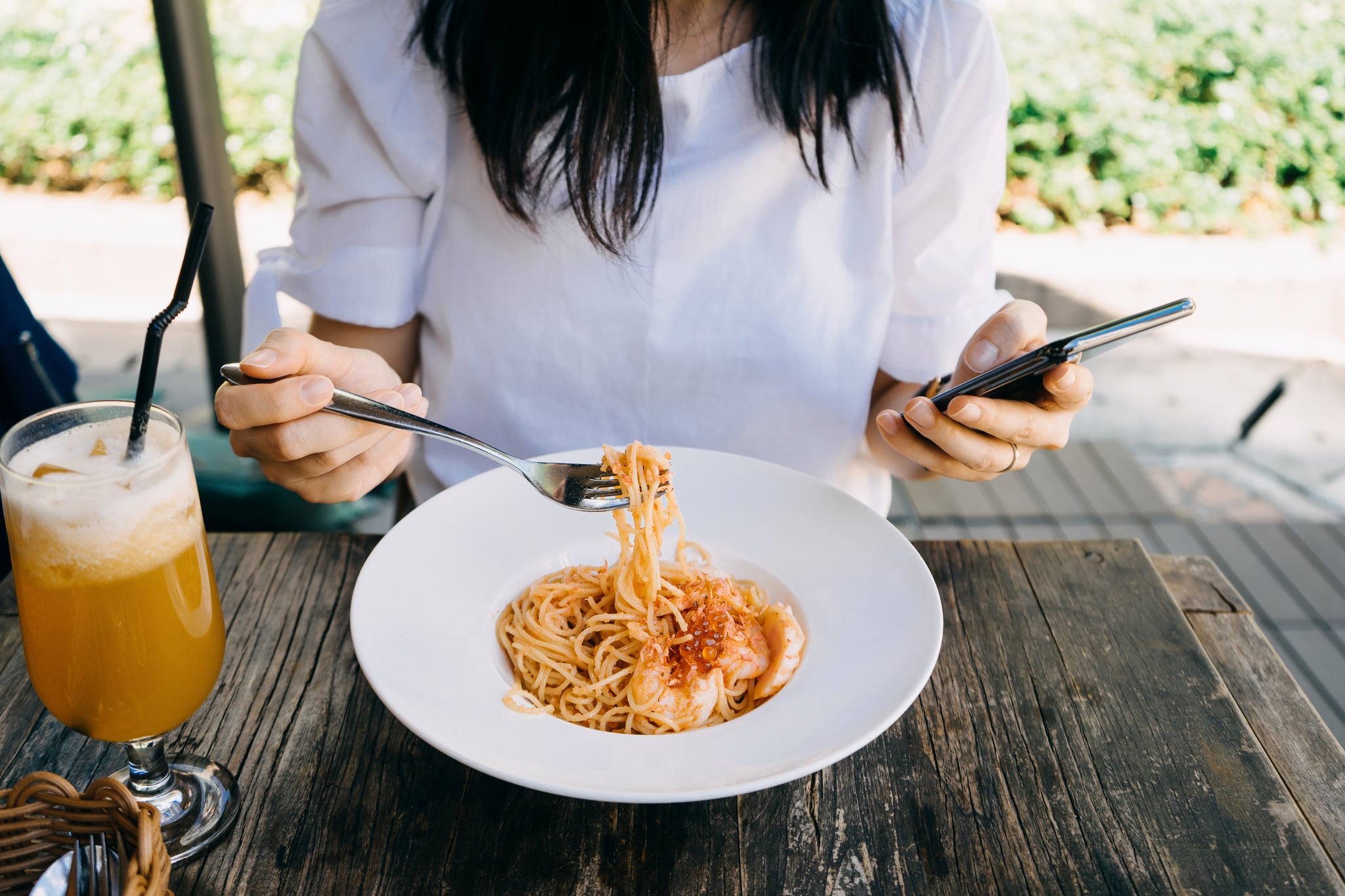 Close up of young woman checking her mobile phone while having meal at a cafe outdoors