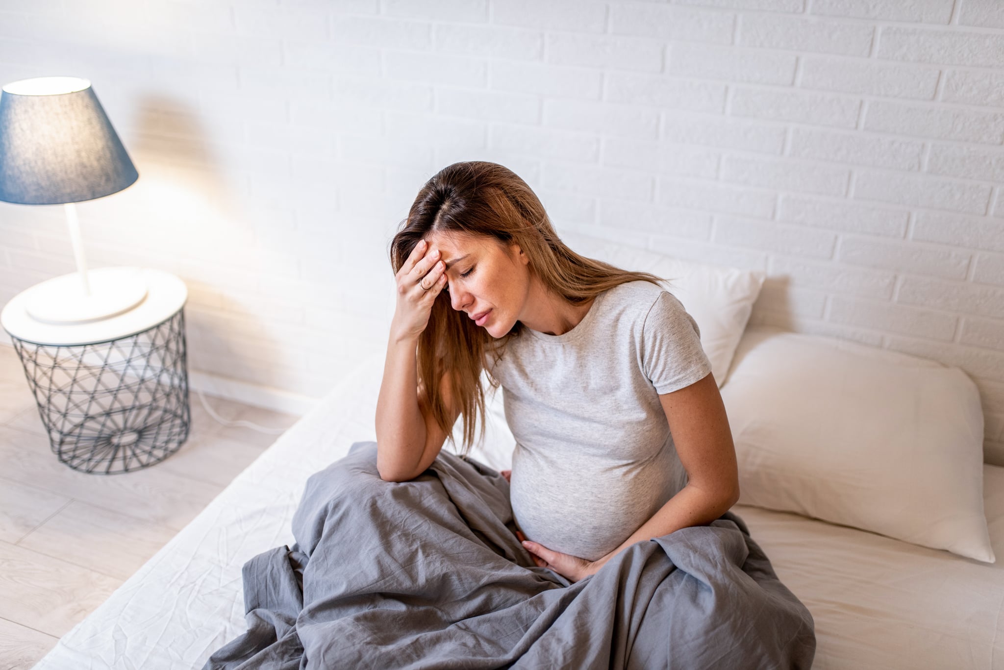 Young pregnant woman having headache. She is resting on bed in the bedroom and feeling unwell.