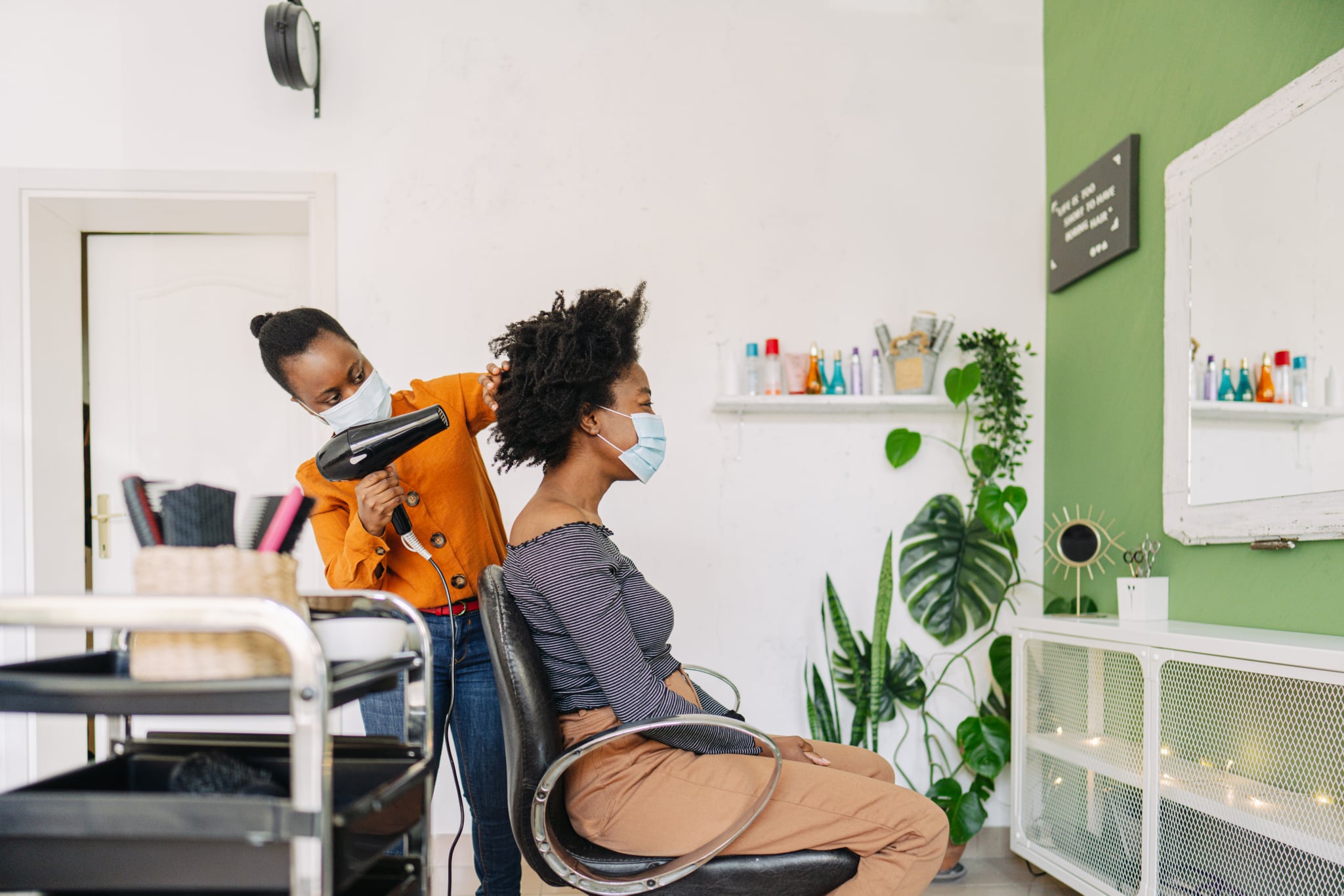 Photo of a young male hairdresser blow-drying hair and wearing protective equipment during the COVID-19 pandemic; visiting hair salons after a long period of lockdown.