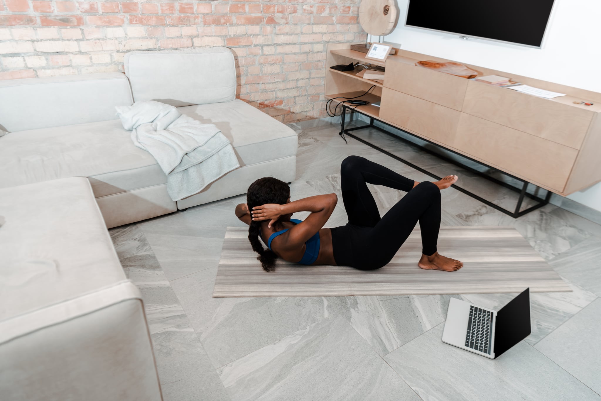 High angle view of african american sportswoman doing abs on yoga mat near laptop in living room