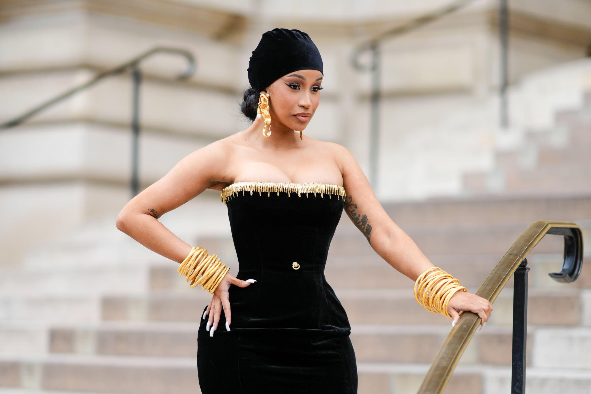 PARIS, FRANCE - JULY 03: Cardi B wears a black velvet scarf as a hat from Schiaparelli, gold large ears and white pearls pendant earrings from Schiaparelli, a black velvet with embroidered gold metallic shoulder-off borders / long tube dress from Schiaparelli, gold large bracelets from Schiaparelli, outside Schiaparelli, during the Haute Couture Fall/Winter 2023/2024 as part of  Paris Fashion Week on July 03, 2023 in Paris, France. (Photo by Edward Berthelot/Getty Images)