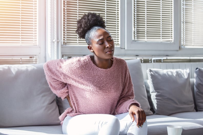 Woman in a pink sweater suffering from lower back pain while sitting on her gray couch.