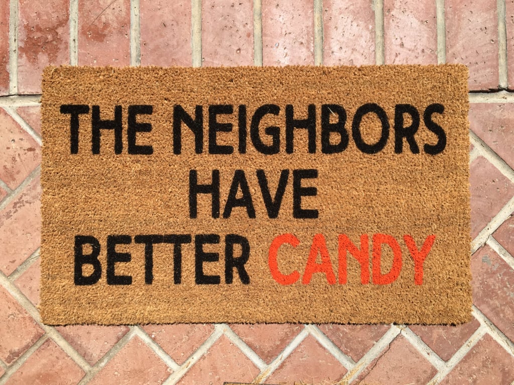 حصيرة باب عليها عبارة The Neighbors Have Better Candy (بسعر 28$ دولار أمريكيّ؛ 103 درهم إماراتيّ/ريال سعوديّ)