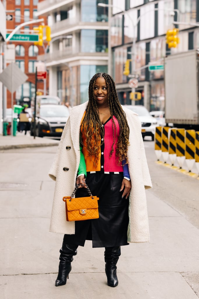 Jessica Andrews wears a vibrant color block ribbed Christopher John Rogers cardigan and a Tibi skirt from Hampden, an orange quilted Chanel bag from Vivrelle, black boots from Flor de Maria, and checkered nails from B-Clawed.