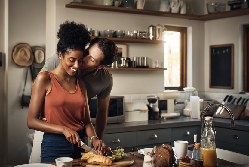 Cropped shot of an affectionate middle aged man kissing his wife on the cheek while she prepares breakfast in their kitchen at home