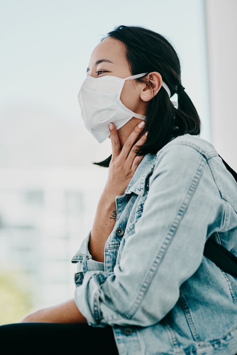 Shot of a young woman wearing a mask and suffering from throat pain in a doctor's office