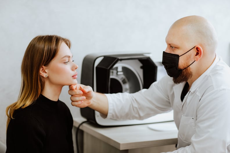 Bold male doctor in black medical mask talking with young female patient in the cabinet. Doc is touching woman's face.Cosmetology concept.